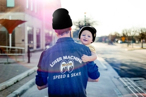 Father and child wearing black knitted beanies with smiley face patch in street setting