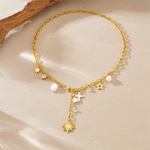Collana a Y dorata con ciondoli a croce stella sole e perle finte su sfondo di sabbia