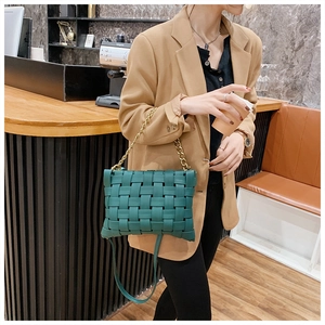Detail of dark green woven leather texture and gold chain handle on a stylish handbag
