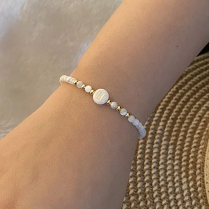 Beaded initial H bracelet with white pearls and gold accents worn on a female wrist