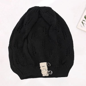 Detail view of a black knit beanie with hollow leaf pattern and lace button trim.