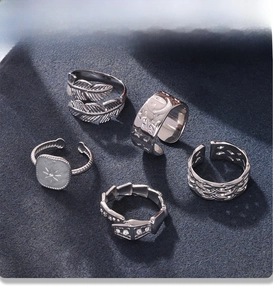Detailed view of five silver adjustable PVD rings featuring feather and star patterns