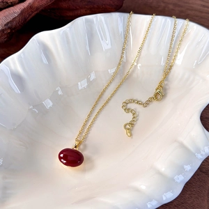 Detailed view of a deep red bean pendant on a delicate gold chain in a shell dish