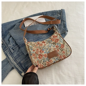 Detail of floral tapestry armpit bag with leather patch and adjustable strap on denim