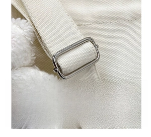 Detail of adjustable strap with metal buckle on off-white canvas shoulder bag