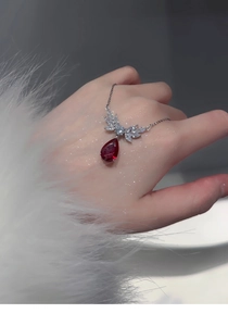 Detailed view of silver necklace with large red teardrop gemstone and zircon angel wings