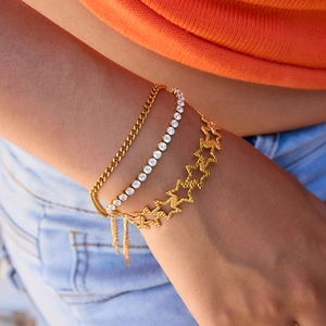 Close-up of stacked gold star bracelets and rhinestone tennis chain on a person's wrist