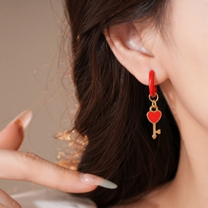 Detailed view of heart-shaped key pendant earring with red enamel on model