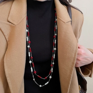Close-up of double-layered long necklace with red beads and pearls on black sweater