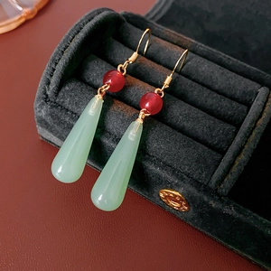 Detailed shot of green resin teardrop earrings with red beads on black velvet tray