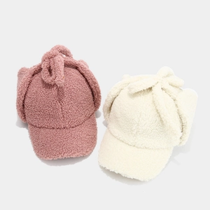 Winter lamb wool earflap hats in pink and white with decorative bow ties on top