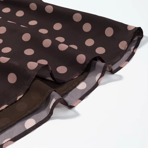 Detail eines kaffeebraunen Chiffon-Tops mit rosa Punkten und gestuftem Rüschensaum