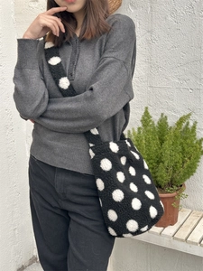 Détail d'un sac à bandoulière en peluche à pois noirs et blancs porté par un modèle