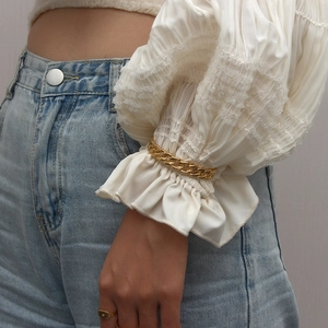 Close-up of a chunky gold chain bracelet and minimalist ring worn with lace sleeve