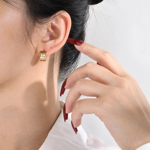 Close-up of a gold square zircon earring worn by a model in a minimalist luxury style