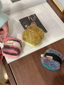 Three colorful plush square AirPods cases with zipper and pearl charms on a magazine