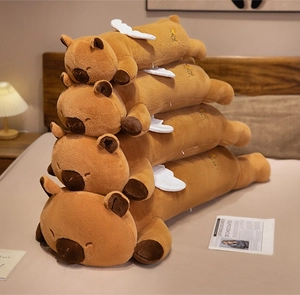 Stack of four brown capybara plush pillows with white wings and flower embroidery detail