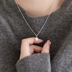 Macro detail of silver heart pendant with textured finish on a beaded chain necklace