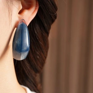 Close-up of a blue resin teardrop earring with natural textures worn by a female model
