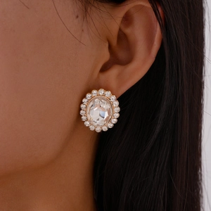 Detailed close-up of golden oval rhinestone earrings with clear faceted crystal