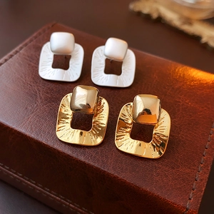 Close-up of gold and silver textured square drop earrings on brown leather background