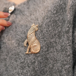Detailansicht einer goldenen Katzenbrosche mit Vintage-Gravur auf einem grauen Pullover