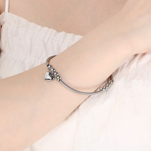 Bracelet jonc argenté avec tube incurvé et pendentif cœur porté par un mannequin