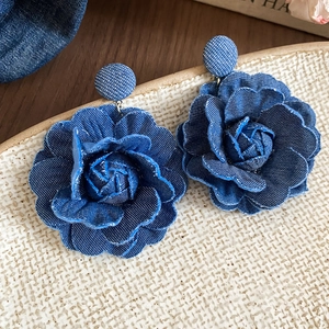 Macro detail of dark blue denim flower earrings with layered petals on a textured dish