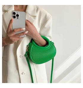 Macro view of emerald green pleated saddle bag with ring handle and elegant crossbody strap