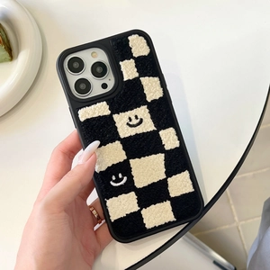Close-up of plush black and white checkerboard phone case with embroidered smileys