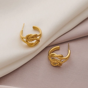 Close-up of golden hammered C-shaped sunflower knot earrings on soft silk fabric