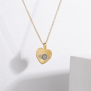 Detail of gold heart pendant necklace featuring micro-set blue zircon evil eye on white background