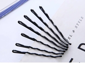 Close-up of seven black wavy metal hair pins arranged on a minimalist white card