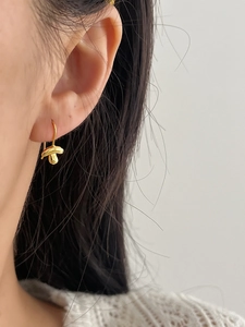 Close-up of a polished gold mushroom-shaped earring worn on a model's ear