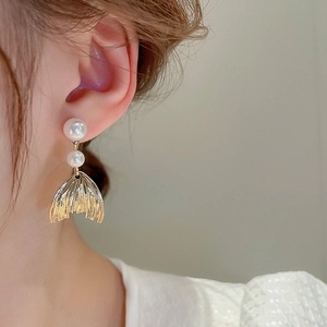 Detail shot of golden fishtail earrings with dual white pearls on a model ear