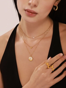 Detail of layered gold necklace with shell pendant, star charm, and bow rings on model