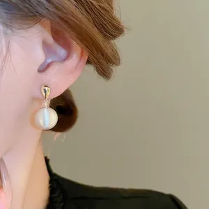 Élégantes boucles d'oreilles goutte d'or avec perles blanches portées par un mannequin