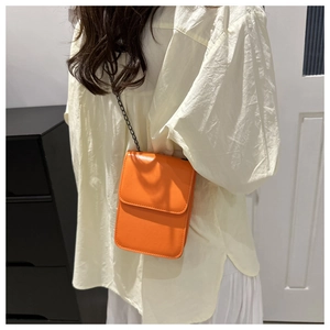 Detail of a bright orange crossbody bag with a black metal chain strap and flap closure