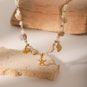 Golden sea shell and starfish pendant necklace with colorful beads on white stone background