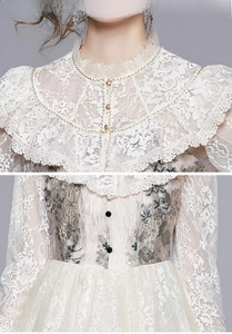Detail of white lace dress featuring high collar, gold chain, and floral embroidery
