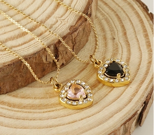 Close-up of gold heart necklaces with pink and black zircon stones on a rustic wood base