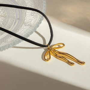 Macro shot of gold bow-knot pendant with black velvet cord on minimalist stone surface