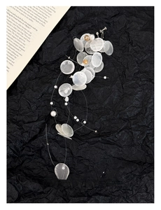 Detail of shell disk and pearl tassel earrings with clip-on design on a paper background