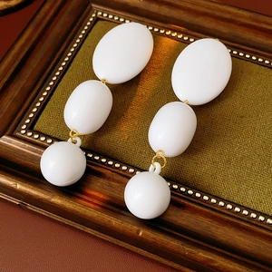 Detail of elegant gold drop earrings with white vintage oval beads on a leather surface