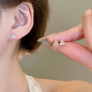 Close-up of golden three-diamond flower stud earrings showing fine craftsmanship on ears