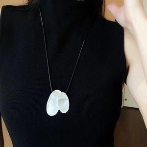 Detail of irregular matte silver pendant on black cord over dark knit sweater