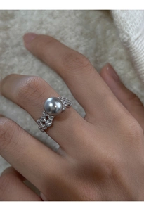 Close-up of a silver ring with a grey pearl and clear zircons on a finger