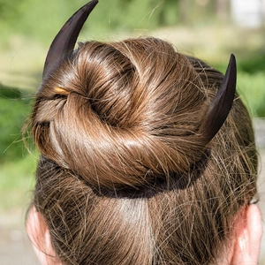 Close-up of a pair of black moon-shaped wooden hair forks styled in a brown hair bun
