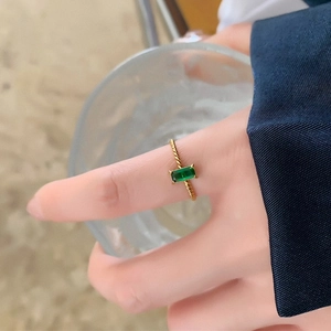 Golden twist band ring with rectangular emerald gemstone worn on a woman's finger