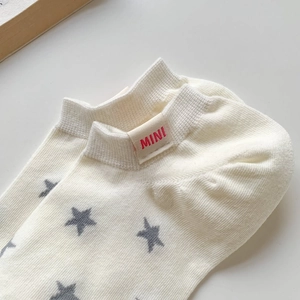 Close-up of off-white cotton star pattern sock with red mini label on white background